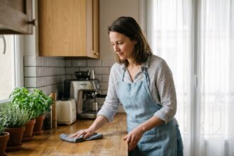 Prestataire de ménage à domicile essuyant un plan de travail en bois dans une cuisine moderne d'appartement français